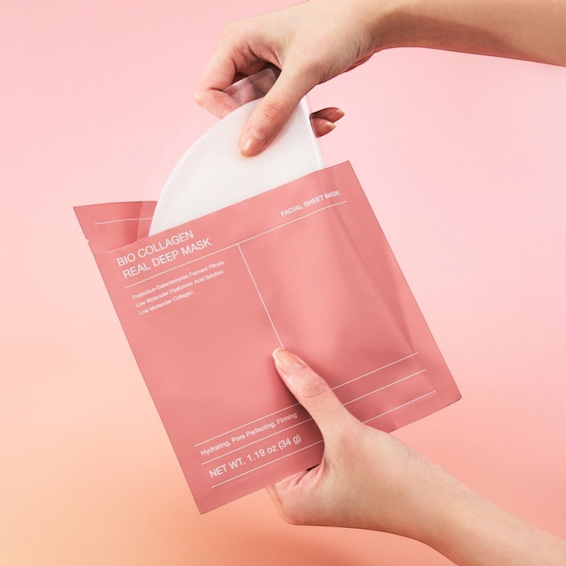 Hands opening a pink BIODANCE Bio-Collagen Real Deep Mask packet against a soft gradient background.
