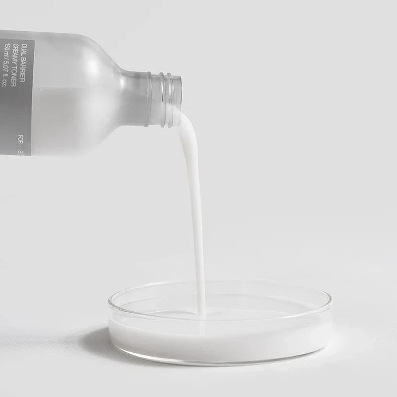 Celimax Dual Barrier Creamy Toner pouring from a frosted glass bottle into a petri dish on a white background