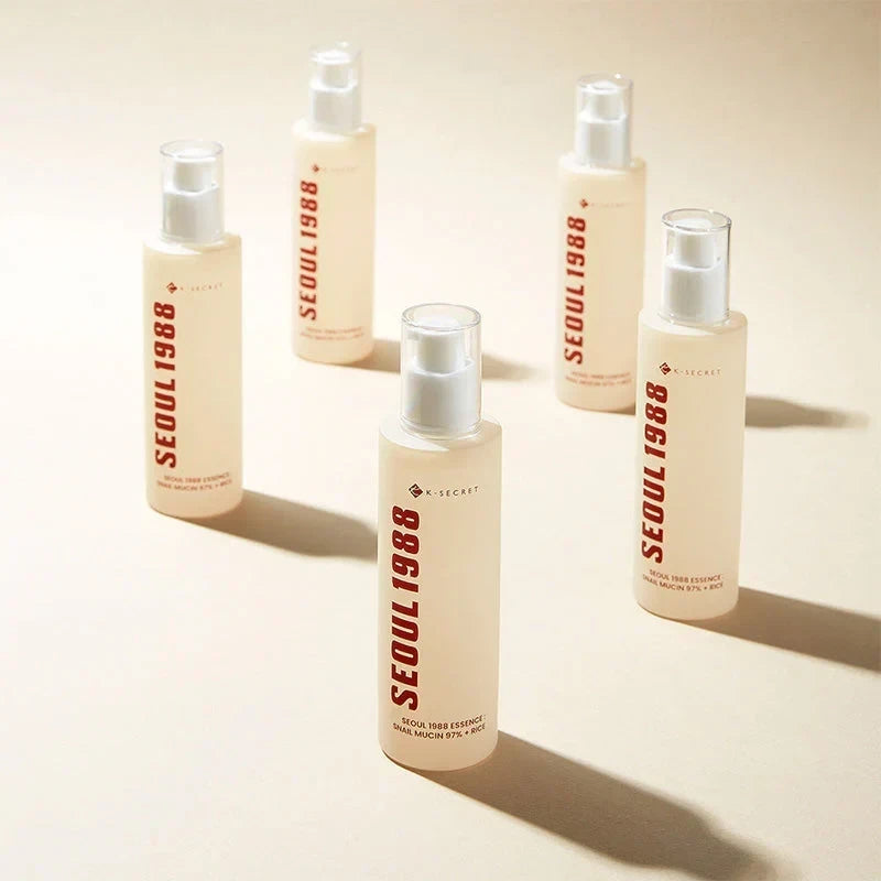 Five bottles of KSECRET SEOUL 1988 Essence with snail mucin and rice, sold by bareskin.lt, on a beige background.