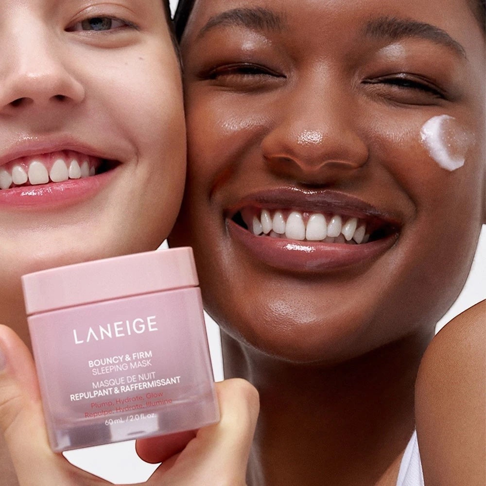 Two smiling women holding a jar of Laneige Bouncy & Firm Sleeping Mask from bareskin.lt for hydrated, firm skin.