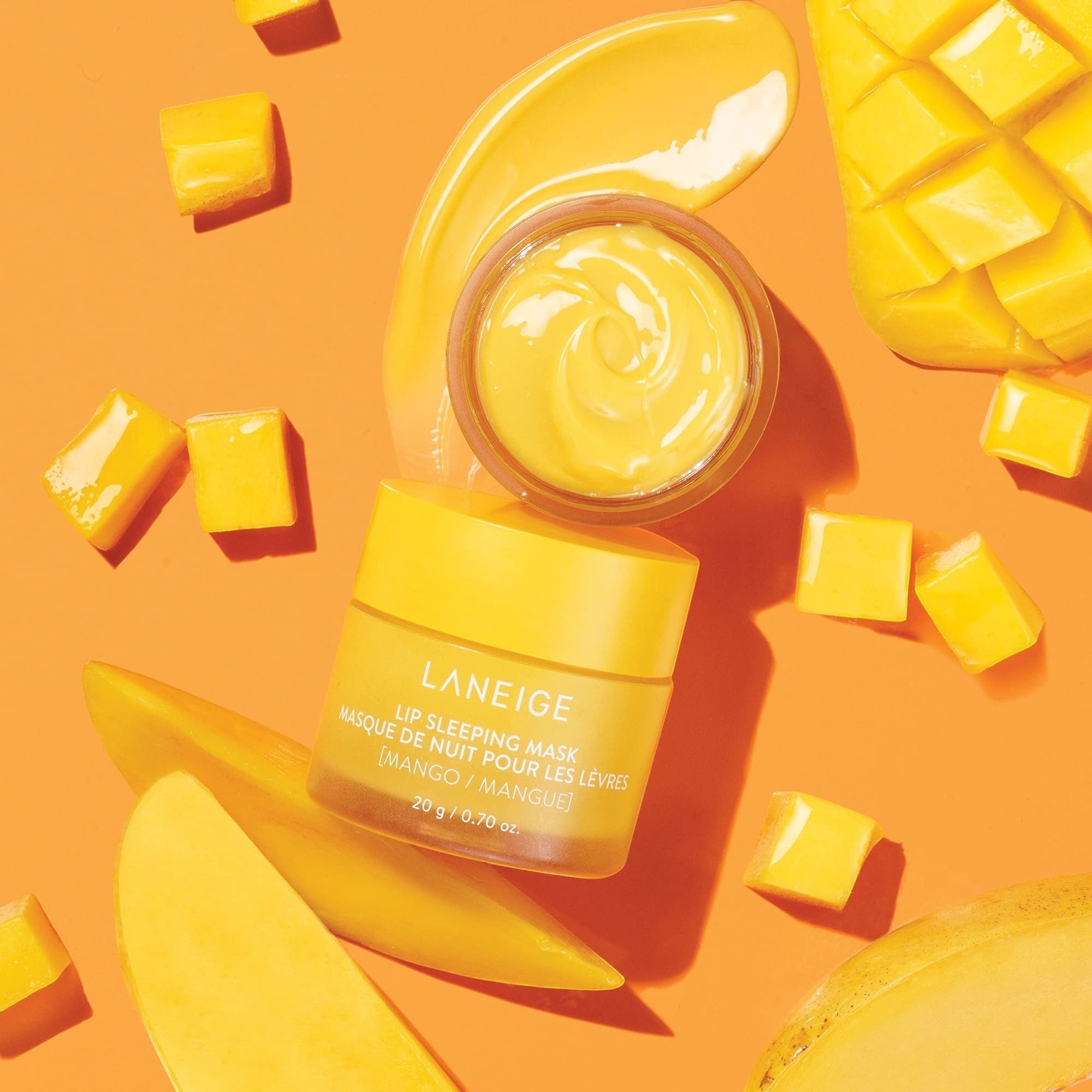 bareskin.lt LANEIGE Mango Lip Sleeping Mask in a yellow jar surrounded by fresh mango slices on an orange background.