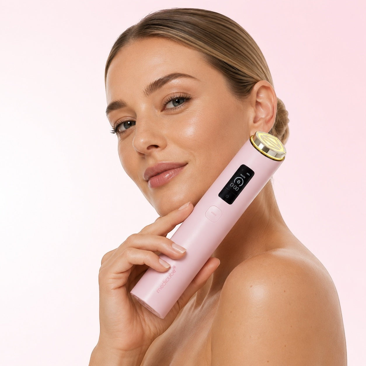 Woman holding a pink Medicube AGE-R Booster Pro skincare device against her cheek for facial rejuvenation