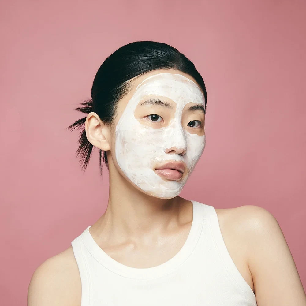 Woman wearing Purito Multi Pdrn Collagen Real Glow Mask on her face against a pink background from bareskin.lt