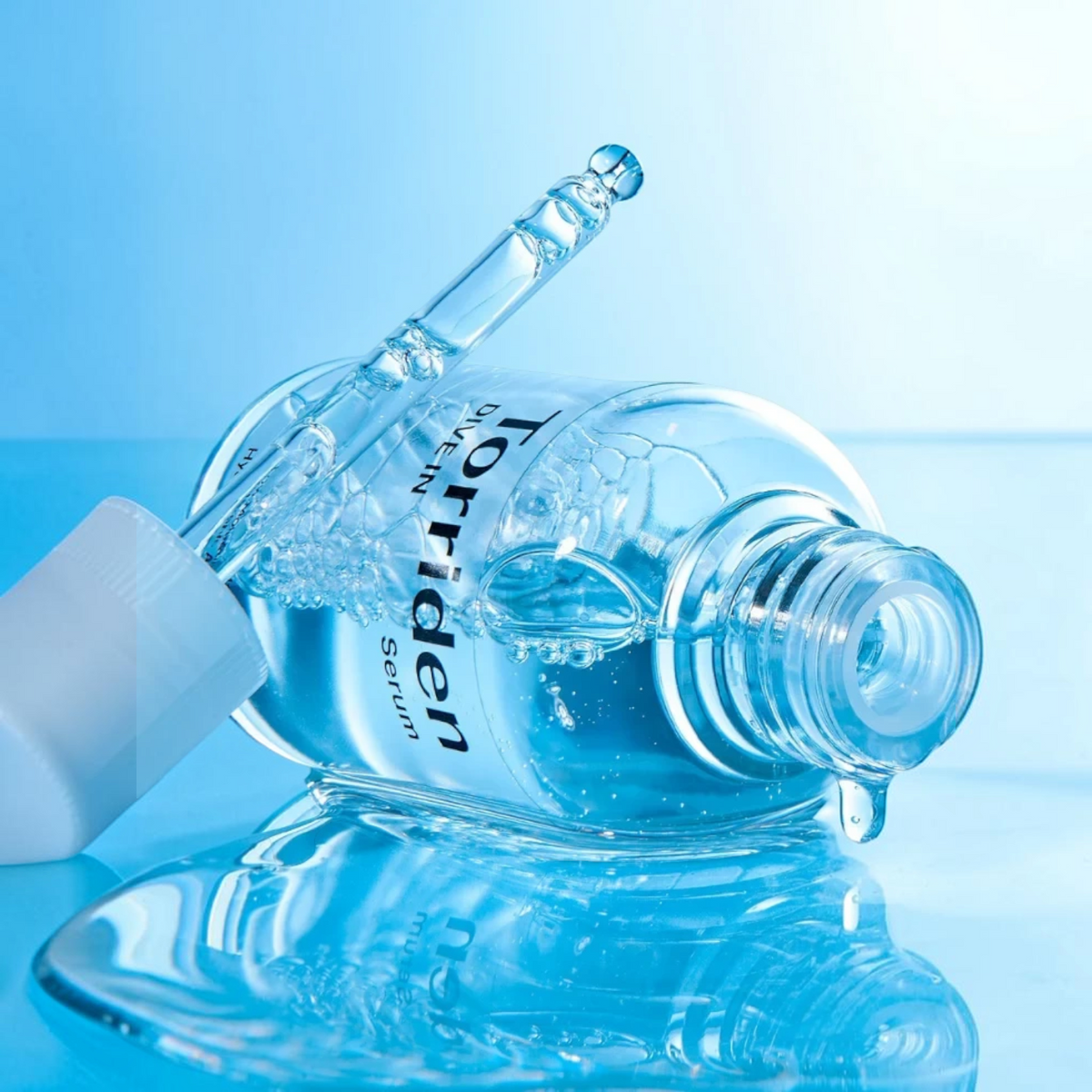 bareskin.lt Torriden DIVE-IN hyaluronic acid serum in a clear glass bottle with a dropper on a blue reflective surface