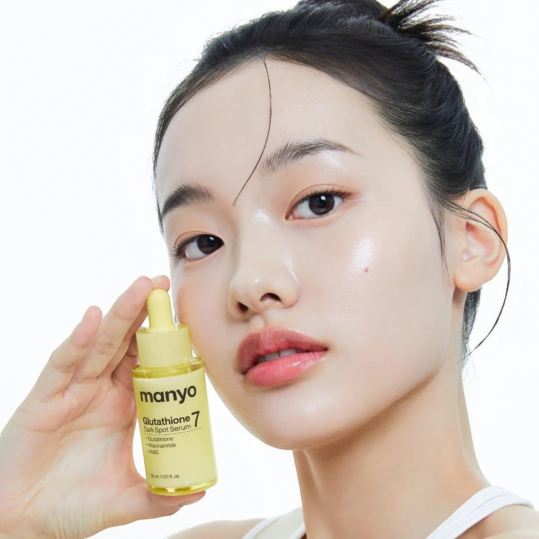 Model holding Manyo Glutathione 7 Dark Spot Serum from bareskin.lt, featuring a yellow bottle for brightening skin.